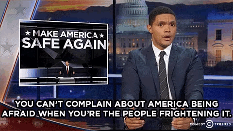 a man in a suit and tie is standing in front of a sign that says make america safe again