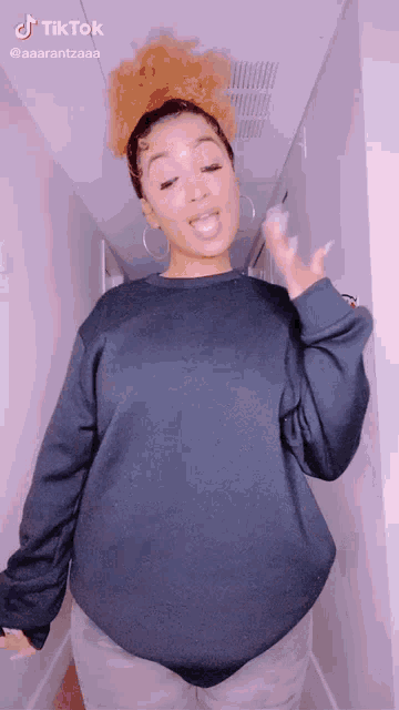 a woman wearing a black sweater and hoop earrings is dancing in a hallway ..
