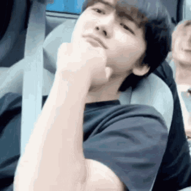 a young man is sitting in a car with his hand on his chin and looking at the camera .