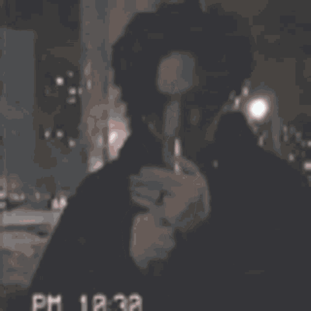 a man is smoking a cigarette in a dark room with a black shirt on .