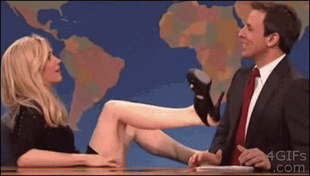 a man in a suit and tie is talking to a woman with her legs crossed in front of a map ..