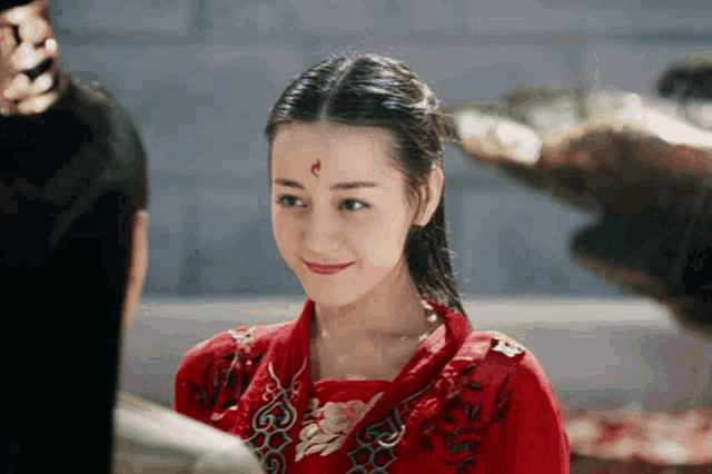 a woman in a red dress with a red flower on her forehead is smiling