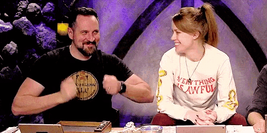 a man and a woman are sitting at a table and the woman is wearing a shirt that says " everything is awful "