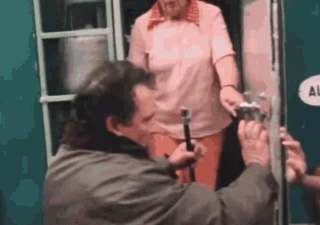 a man is fixing a door with a hammer while a woman stands behind him .