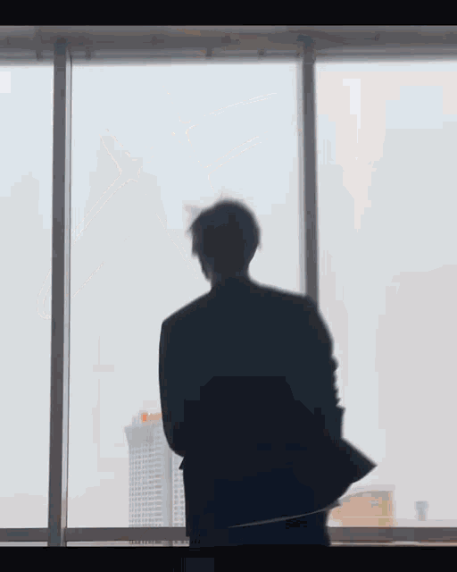 a man in a suit is standing in front of a window and looking out .