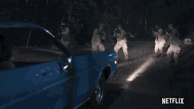 a group of soldiers standing next to a blue car with netflix written on the bottom