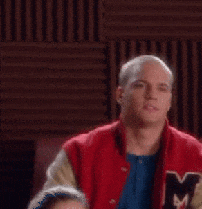 a man wearing a red varsity jacket with the letter m on it is looking at the camera .