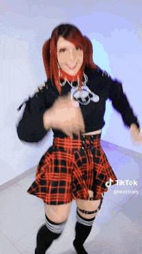 a woman wearing a plaid skirt and a choker is dancing in a room .