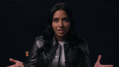 a woman wearing a black leather jacket is sitting in a chair with her hands outstretched