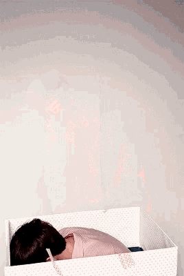 a man in a pink shirt is laying down in a box .