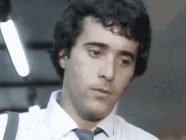 a man with curly hair and a white shirt and tie is looking at the camera .