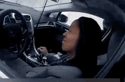 a woman is sitting in the driver 's seat of a car and holding the steering wheel .