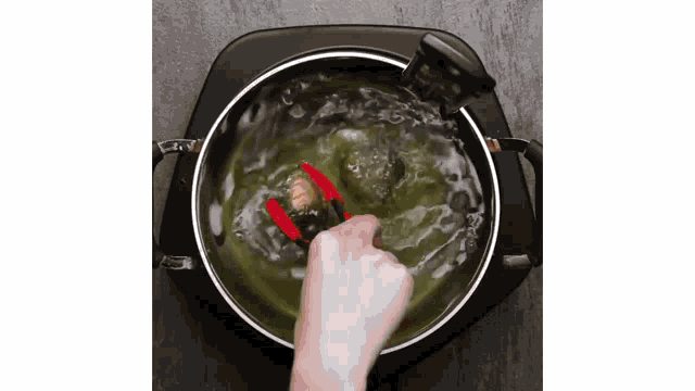 a person is using tongs to stir a pot of water .