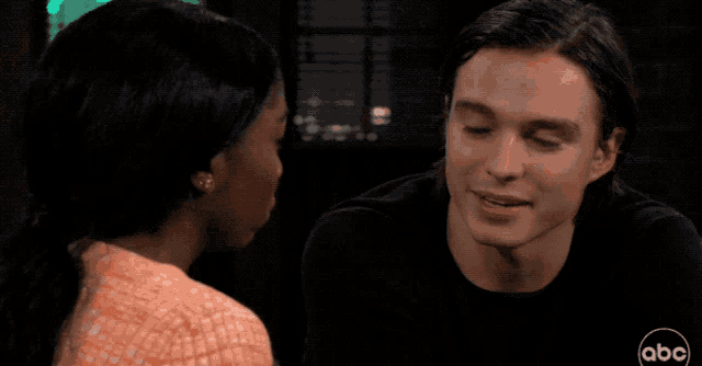 a man and a woman are looking at each other in front of a brick wall with abc written on the bottom