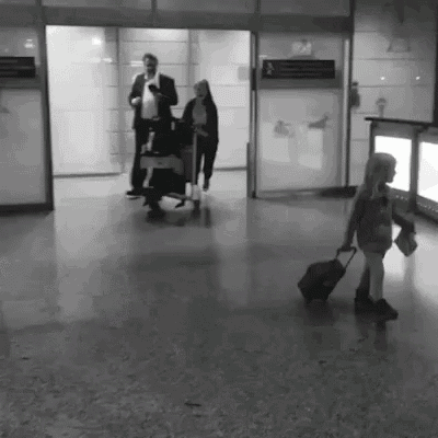 a black and white photo of a little girl walking with a suitcase in an airport