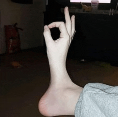a person is sitting on the floor with their foot up and making a ok sign with their hand .