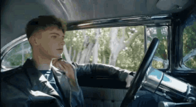 a young man is sitting in the driver 's seat of a car and looking out the window .