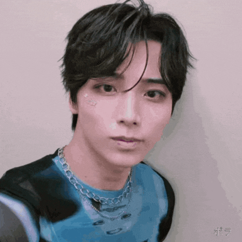 a close up of a young man wearing a blue shirt and a necklace