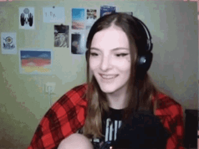 a girl wearing headphones and a plaid shirt is smiling while sitting in front of a microphone .