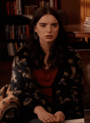 a woman is sitting at a table wearing a leopard print jacket and earrings .