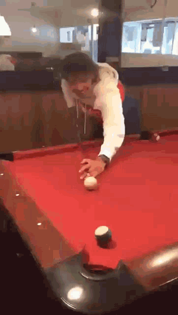 a man in a white hoodie is playing pool on a red table
