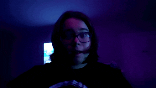 a woman wearing glasses and a black shirt with a skull on it is standing in a dark room