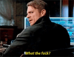 a man in a black jacket is sitting in front of a computer screen and asking what the fuck .