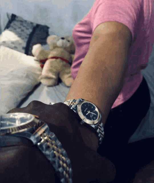 a woman in a pink shirt is holding a teddy bear while a man wearing a watch shows the time as 4:20