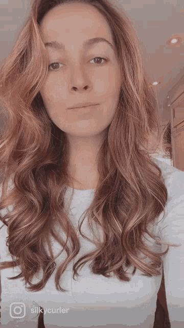 a woman with long brown hair is wearing a white shirt with silkycurler on the bottom right