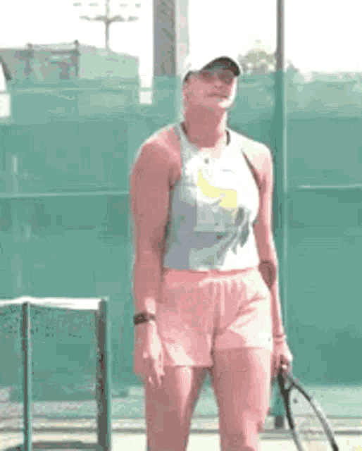 a woman in a tank top and pink shorts is holding a tennis racquet on a tennis court .