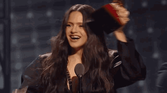 a woman in a black jacket is holding a red brush in front of a microphone and smiling .