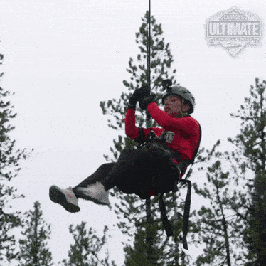 a man in a red shirt is hanging from a rope with a canada ultimate challenge logo behind him