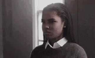 a woman with dreadlocks is wearing a sweater and a white shirt and looking at the camera .