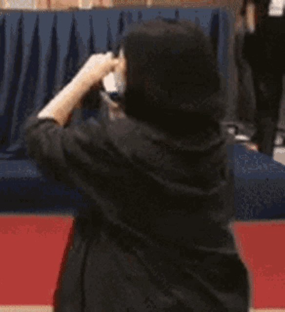 a woman in a graduation cap and gown is standing on a red carpet in front of a blue curtain .