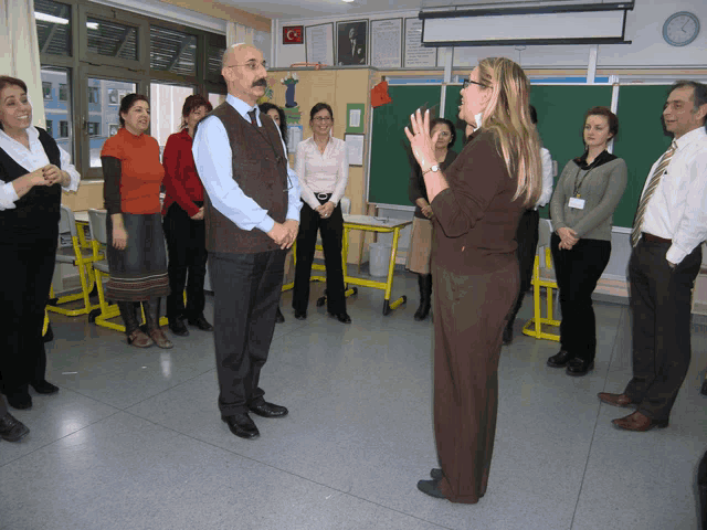 a group of people standing in a classroom with a clock on the wall above them