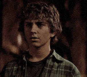 a young man with curly hair wearing a green plaid shirt looks at the camera