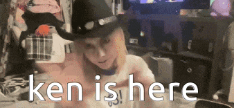a man wearing a cowboy hat says " ken is here " in a room