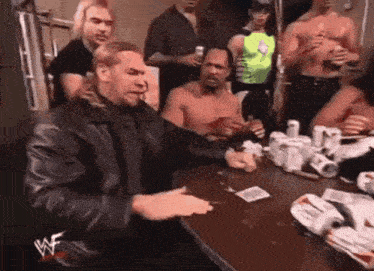 a man in a leather jacket is sitting at a table with a group of men playing cards .