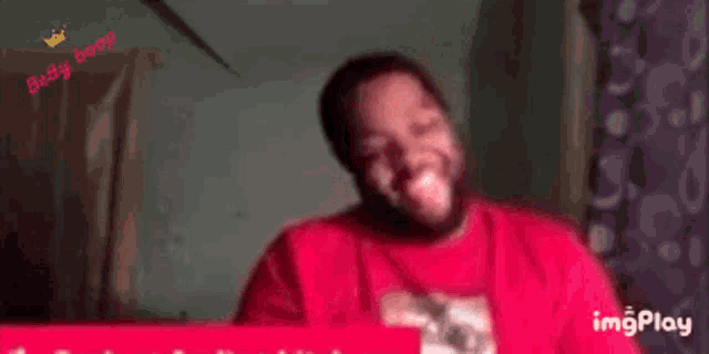 a man in a red shirt is making a funny face with his hands on his ears .