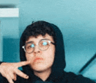 a young man wearing glasses and a black hoodie is making a peace sign .