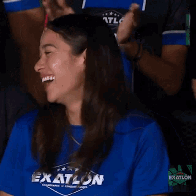 a woman wearing a blue shirt with the word exatlon on it is smiling and clapping .