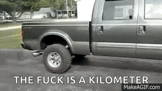 a pickup truck is driving down a road with the words `` the fuck is a kilometer '' written on the bottom .