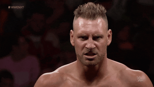 a man with a beard stands in front of a crowd with the hashtag #wwe nxt