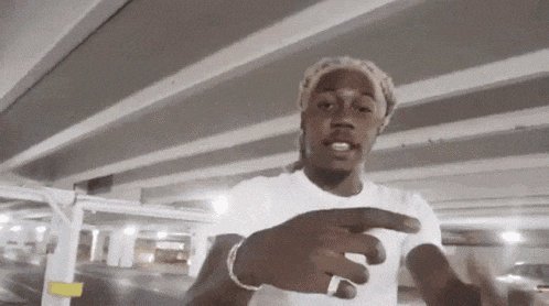 a man wearing a white shirt and a ring is standing under a bridge in a parking garage .