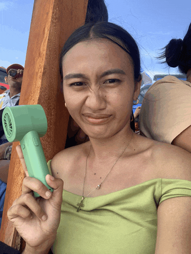 a woman in a green off the shoulder top is holding a small green fan