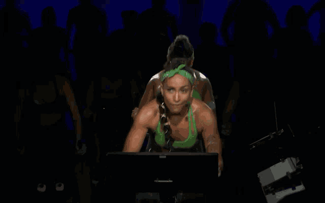 a woman in a green top is riding an exercise bike in front of a monitor