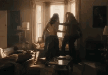 two women are fighting in a living room with a couch .