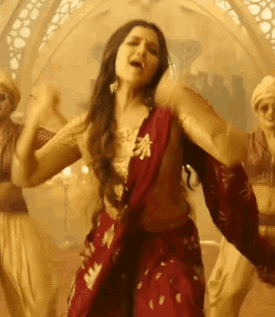 a woman in a red saree is dancing in a room with other people .