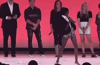 a group of people standing on a stage with a woman dancing in front of them