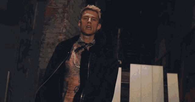 a man with a tattoo on his chest is standing in front of a brick wall with his arms outstretched .